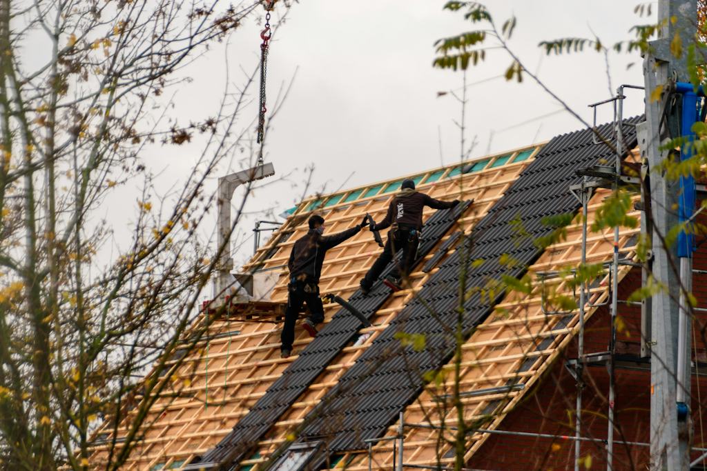Two roofers setting dark tiles on an open roof frame