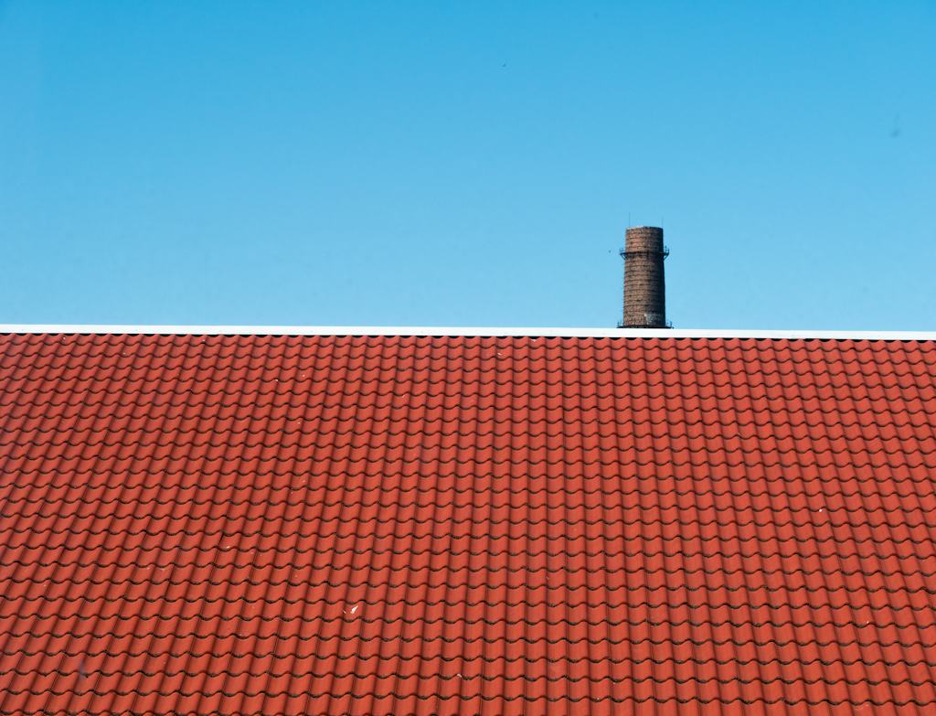 Red clay tile roof and brick chimney under a clear sky